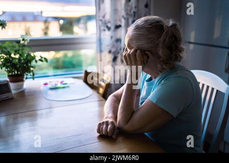 Donna anziana triste. Donna anziana depressa e solitaria con alzheimer, demenza, perdita di memoria o solitudine. Persona anziana che guarda fuori dalla finestra di casa. Foto Stock