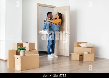 Gioioso marito nero che porta moglie entrando a casa dopo il trasferimento al coperto Foto Stock