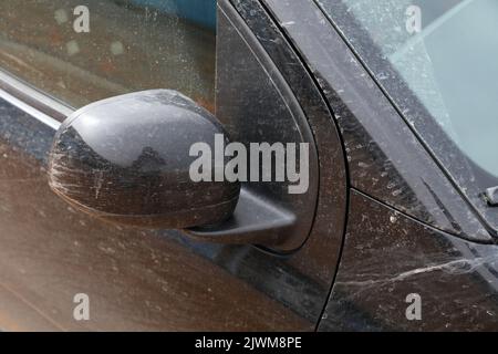 L'auto sporca ha bisogno di un lavaggio. Piccola vettura nera con sporcizia sulla carrozzeria e sullo specchietto laterale. Foto Stock