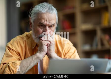 Pensionato concentrato seduto di fronte al notebook a casa Foto Stock