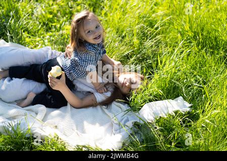 Fratello e sorella abbracciano e ridono felicemente, sdraiati sull'erba verde. Il sole splende, i bambini sono felici spensierati. Il concetto di una vita familiare felice e legame. Spazio di copia. Foto Stock