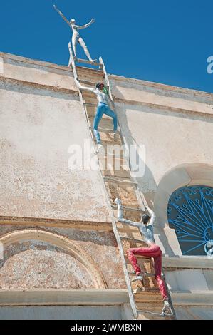 La decorazione dell'edificio non identificato, rappresenta gli uomini clambering sulla scala a pioli e una donna in piedi sulla cima, a Oia, Santornin Grecia Foto Stock