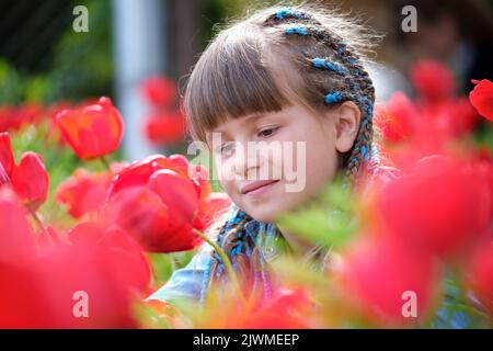 Ragazza felice bambino godendo dolce odore di tulipano rossi fiori in giardino d'estate Foto Stock