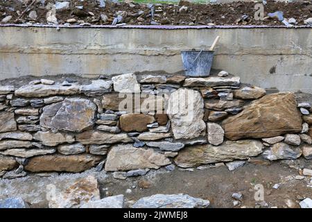 Muratura tradizionale in pietra naturale in Francia. Costruzione di un muro ornamentale in pietra di gneiss. Foto Stock