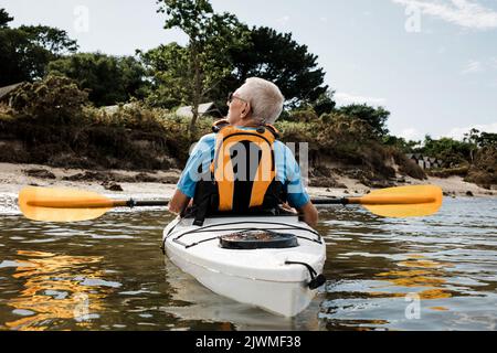 Uomo in pensione fuori in mare esercitandosi su un kayak nella costa Dorset Foto Stock