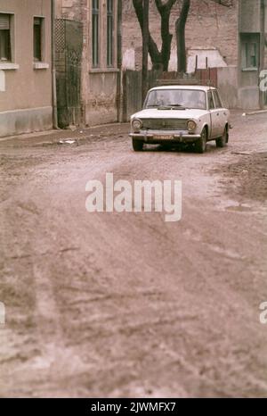 Bucarest, Romania, gennaio 1990, poche settimane dopo la caduta del comunismo. Mentre Ceausescu si concentrava sulla costruzione dei suoi progetti megalomanici, come il Centro Civico, i quartieri storici della capitale si deterioravano lentamente. Alcune case storiche nelle vicinanze del Blvd. Della Vittoria del socialismo sono state evacuate per demolizione, e a malapena sfuggite grazie alla Rivoluzione anticomunista. In questa foto, una macchina sta guidando sulle strade fangose nel vecchio quartiere '11 Iunie'. Foto Stock