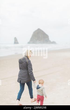 Madre caucasica e figlio bambino camminano lungo Cannon Beach. Foto Stock