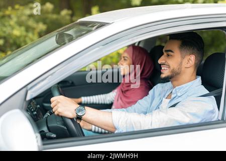 Felice moglie musulmana millenaria in hijab e marito guida l'auto al volante, godere di viaggio Foto Stock