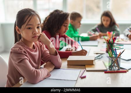 Infelice Asian Schoolgirl pensare seduta con diversi compagni di classe in classe Foto Stock