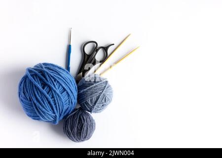 Palline blu di filo da maglieria con forbici, uncinetto e aghi da maglieria su fondo bianco per hobby. Piatto, isolato Foto Stock