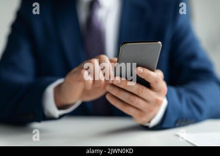 Immagine ritagliata di un uomo d'affari in tuta utilizzando lo smartphone sul luogo di lavoro Foto Stock