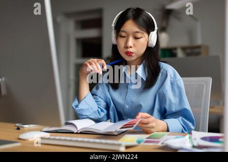 Coreano Lady Designer lavorare con Color Palettes vicino computer Indoor Foto Stock