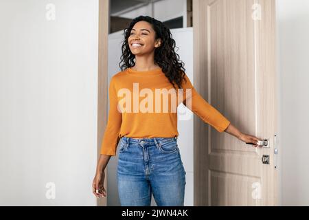 Felice giovane donna nera che entra l'appartamento che apre la porta di ingresso Foto Stock