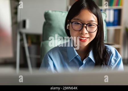 Happy Asian Businesswoman utilizzando computer indossando auricolari seduti in ufficio Foto Stock