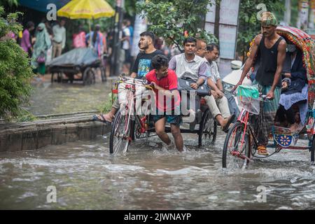 I risciò trasportano i passeggeri e cercano di farli attraversare le strade di Dhaka, affondate d'acqua, dopo una forte pioggia di monsoni. Le forti piogge monsoniche causano il disboscamento delle strade, le strade sono parzialmente sommerse rendendo i viaggi pericolosi. Foto Stock