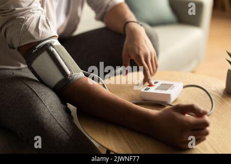 Primo piano di un giovane uomo nero che controlla la pressione sanguigna, utilizzando un moderno tonometro a casa Foto Stock