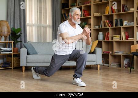 Un anziano atletico motivato che fa affondi a casa Foto Stock