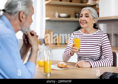 Donna anziano felice che beve il succo mentre ha fatto colazione con il marito in cucina Foto Stock