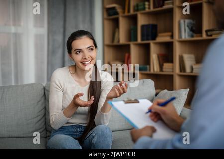 Sorridente giovane donna europea paziente parlando, gesturing con medico maschile in clinica ufficio interno Foto Stock