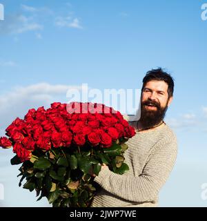 Uomo con bouquet di fiori. Happy man tiene un grande bouquet di rose rosse, proporre al fidanzato in data. Romantico ragazzo celebrare San Valentino. Foto Stock