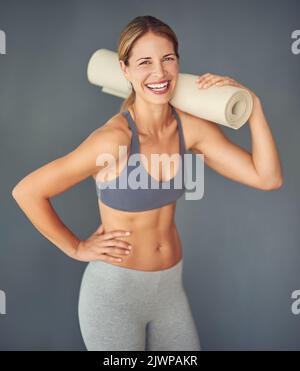 Im in grande forma, grazie allo yoga. Ritratto corto di una donna matura attraente che tiene il suo tappetino yoga. Foto Stock