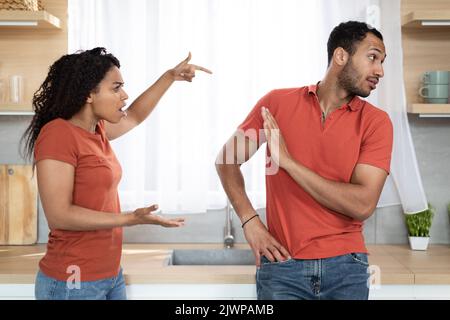 Arrabbiato millenario moglie afroamericana urlando scolding offeso marito in cucina interno Foto Stock