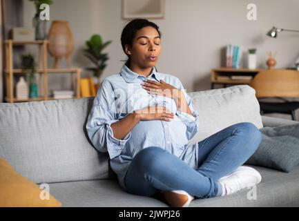 Donna Africana americana incinta che fa esercizio di respirazione seduto a casa Foto Stock