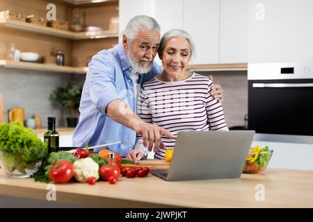 Felice sposato Senior Couple che usa il laptop mentre cucinava cibi sani in cucina Foto Stock