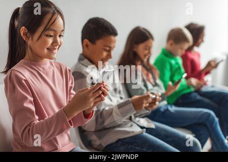 Bambini diversi che utilizzano telefoni Giochi per cellulari su sfondo grigio Foto Stock