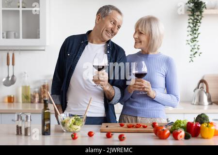 Sposi anziani che amano bere vino mentre cucinano insieme Foto Stock