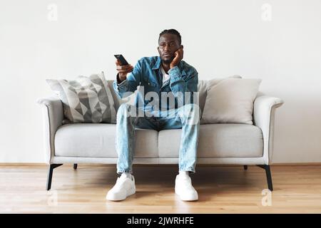 Annoiato Black Guy guardare film in TV seduto a casa Foto Stock