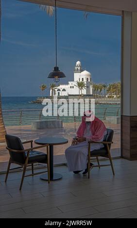 Uomo arabo in caffetteria con moschea isola sullo sfondo Jeddah Corniche Arabia Saudita Foto Stock