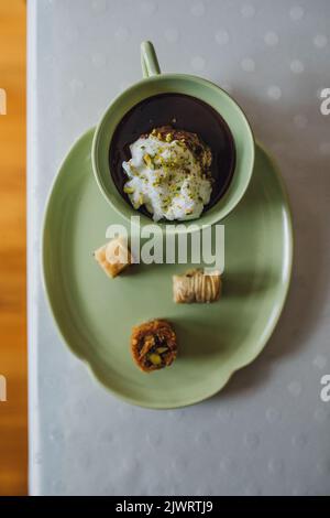 bere il cioccolato in una tazza verde abbinata e piatto con dolci di baklava assortiti su tovaglia bianca a puntini di polka Foto Stock