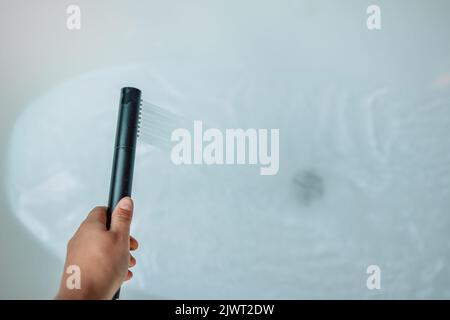 La mano di una donna tiene una doccia e versa l'acqua nel bagno. Acqua blu nel bagno. Bagno. Vista dall'alto. Foto Stock