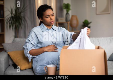 Discontented incinta Donna Nera Holding consegna vestiti Unpacking Box Indoor Foto Stock