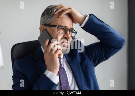Interessato uomo d'affari di mezza età che parla sul cellulare e toccando testa in stress Foto Stock