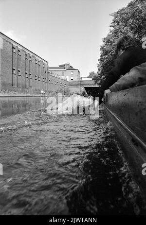 Londra, Inghilterra, circa 1967. Ragazzi del Pirate Club a bordo di una piccola barca sul Regent’s Canal. Un ragazzo sta trascinando le dita attraverso l'acqua. Un pescatore dal towpath guarda sopra. Il Pirate Club, un club nautico per bambini, è stato fondato nel 1966 presso Gilbey’s Wharf sul Regent’s Canal vicino a Camden, Londra. La loro clubhouse era una vecchia chiatta e un certo numero di piccole barche e canoe erano state donate per l’uso dei bambini. Foto Stock