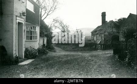 1950s. Un pittoresco villaggio in Cornovaglia, Inghilterra. La vista mostra una piccola casa con una finestra baia e un primo cottage con travi in legno circondato da una recinzione per picnic. Foto Stock