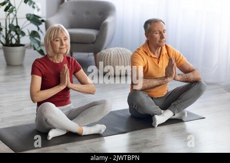 Tranquilla coppia anziana seduta sul tappetino fitness in posa lotus Foto Stock