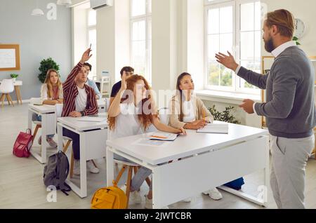 Gli studenti universitari attivi alzano le mani in classe per rispondere alle domande degli insegnanti. Foto Stock