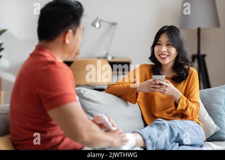 Amando il marito asiatico massaggiare i piedi sorridenti della moglie Foto Stock