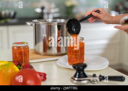 Inscatolamento domestico delle verdure. Una donna in primo piano conserva un'insalata di verdure in un vasetto di vetro Foto Stock