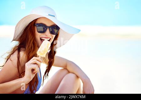 Adoro le estati ricche di gelato. Ritratto di una bella giovane donna che mangia un gelato in spiaggia. Foto Stock