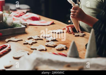 Natale e Capodanno preparazione alimentare. Cucina di pan di zenzero, biscotti decoranti con glassa e mastice. Ragazza piccola decorare cookie. Primo piano sul colpo corto con le mani del bambino del bambino del toddler che tengono la glassa Foto Stock