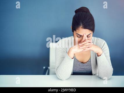 Lo stress sta affondando. Una giovane donna d'affari sopraffatta che tiene la testa tra le mani mentre si siede alla sua scrivania. Foto Stock