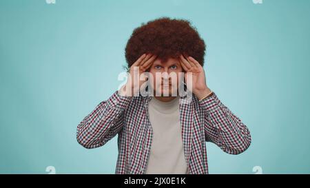 Nosy curioso uomo chiudere gli occhi con la mano e spiare attraverso le dita, nascondere e piangere, gesto binoculare, esplorare il modo, alla ricerca di qualcosa in lontananza. Ragazzo giovane adulto su sfondo blu studio Foto Stock