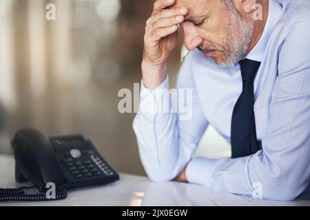 Lo stress sta arrivando a lui. Un uomo d'affari maturo che guarda stressato mentre lavora nel suo ufficio. Foto Stock