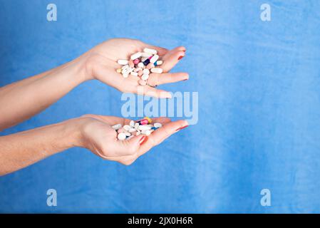 Diverse pillole in una palma persone contro sfondo blu. Forniture mediche. Foto Stock