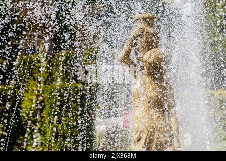 La fontana da vicino si riversa su una statua di una donna. Spruzzi d'acqua e scultura in pietra di una ragazza con caraffa Foto Stock