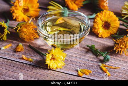 Calendula officinalis olio cosmetico, fiori di palamite essiccati e freschi su tavola di legno Foto Stock